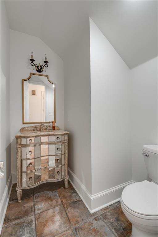 bathroom featuring tile flooring, vaulted ceiling, vanity, and toilet