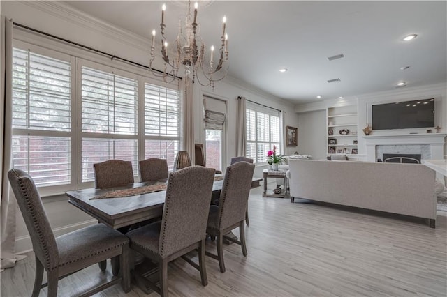 dining space with built in features, light hardwood / wood-style floors, crown molding, and an inviting chandelier