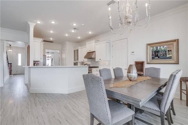 dining space featuring light wood-type flooring, crown molding, an inviting chandelier, and decorative columns