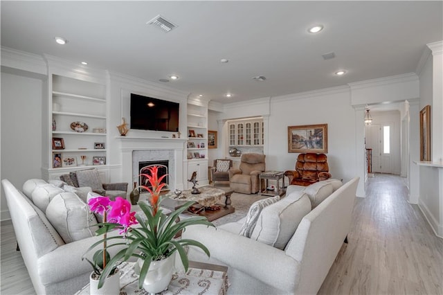 living room featuring ornamental molding, light hardwood / wood-style floors, built in shelves, and a premium fireplace