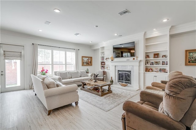 living room with a healthy amount of sunlight, light hardwood / wood-style floors, built in shelves, and a premium fireplace