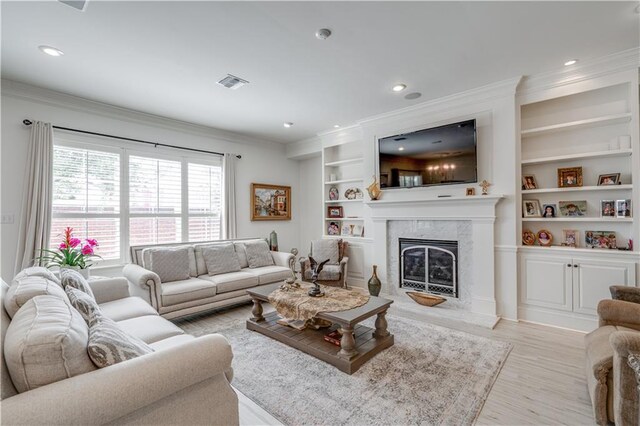 living room featuring ornamental molding, light hardwood / wood-style floors, a high end fireplace, and built in shelves