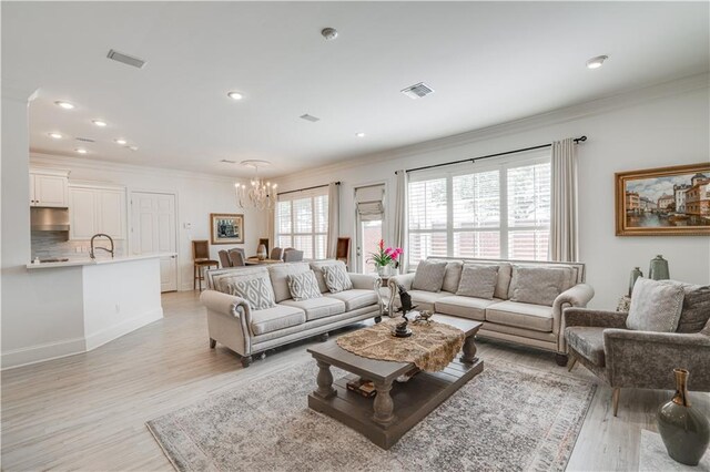 living room featuring sink, an inviting chandelier, crown molding, and light wood-type flooring