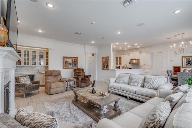 living room featuring light hardwood / wood-style flooring, sink, crown molding, and an inviting chandelier