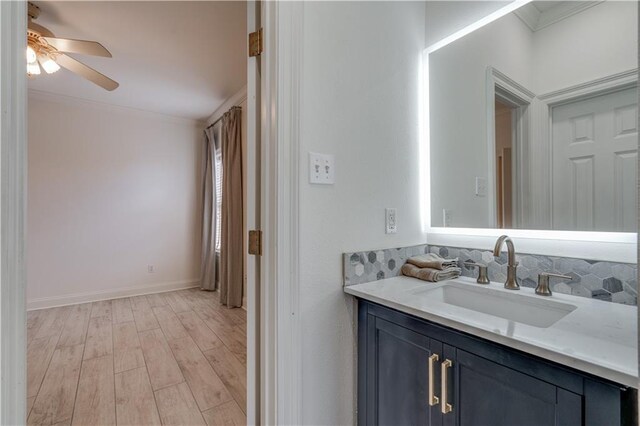 bathroom featuring crown molding, vanity, hardwood / wood-style floors, tasteful backsplash, and ceiling fan