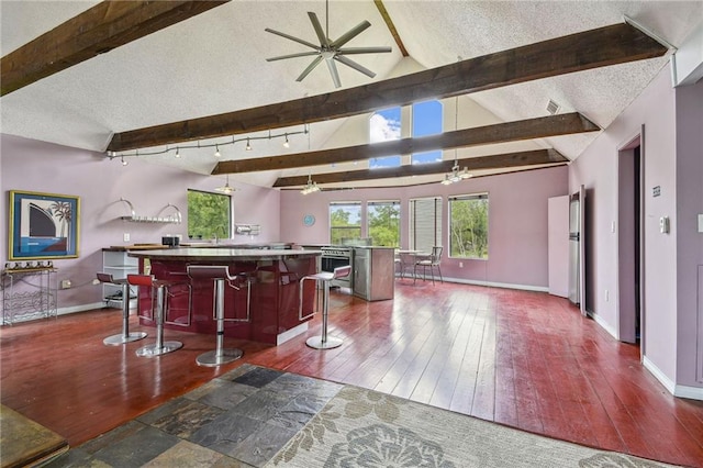 kitchen with ceiling fan, dark hardwood / wood-style floors, lofted ceiling with beams, a center island, and a breakfast bar