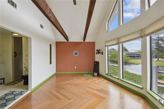 empty room featuring light parquet floors, beamed ceiling, a high ceiling, and a water view