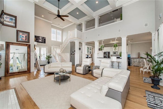 living room featuring ceiling fan, light hardwood / wood-style flooring, decorative columns, coffered ceiling, and a towering ceiling