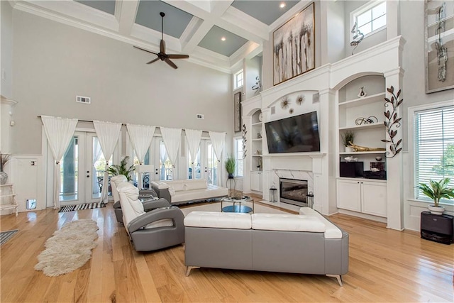 living room with light hardwood / wood-style floors, a high end fireplace, a high ceiling, coffered ceiling, and ceiling fan