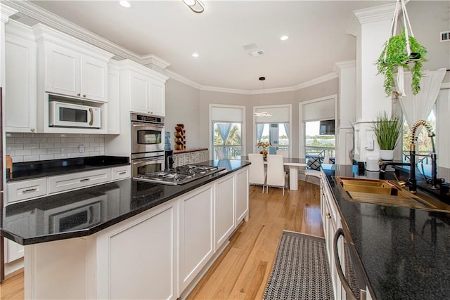 kitchen featuring dark stone counters, tasteful backsplash, light wood-type flooring, white cabinets, and appliances with stainless steel finishes