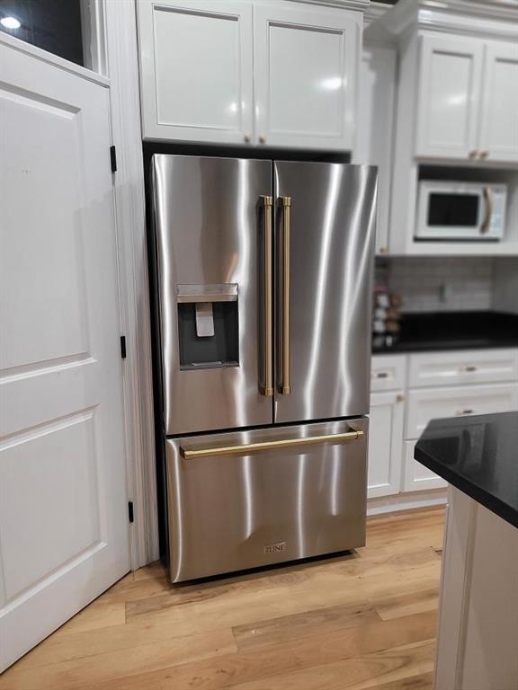 kitchen with light hardwood / wood-style flooring, white cabinets, stainless steel refrigerator with ice dispenser, and white microwave