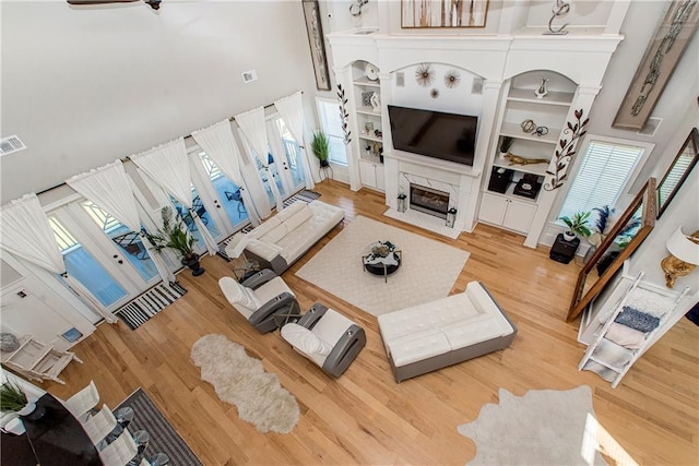 living room featuring a premium fireplace, a towering ceiling, built in shelves, and light wood-type flooring