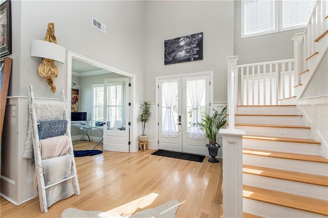 entryway with a towering ceiling, french doors, crown molding, and light wood-type flooring