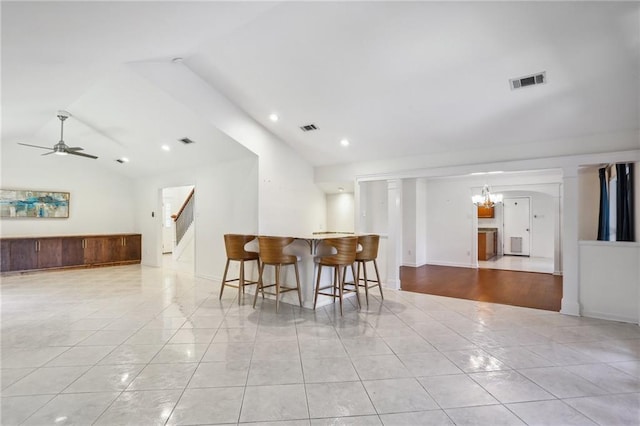 tiled dining area with bar, vaulted ceiling, and ceiling fan with notable chandelier