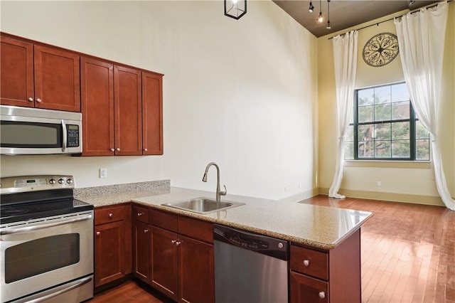 kitchen with light stone countertops, kitchen peninsula, light hardwood / wood-style flooring, stainless steel appliances, and sink