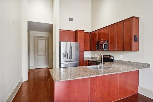 kitchen with light stone counters, appliances with stainless steel finishes, a high ceiling, dark hardwood / wood-style floors, and kitchen peninsula