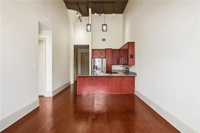 kitchen with kitchen peninsula, decorative light fixtures, stainless steel appliances, a high ceiling, and dark wood-type flooring