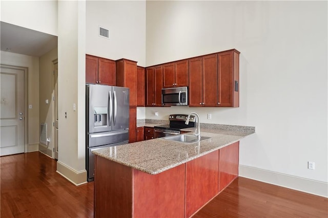 kitchen featuring kitchen peninsula, appliances with stainless steel finishes, dark wood-type flooring, light stone counters, and sink