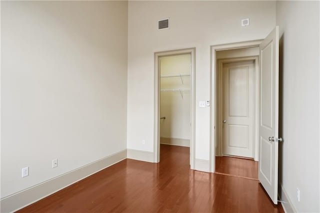 unfurnished bedroom with a closet, a spacious closet, and dark wood-type flooring