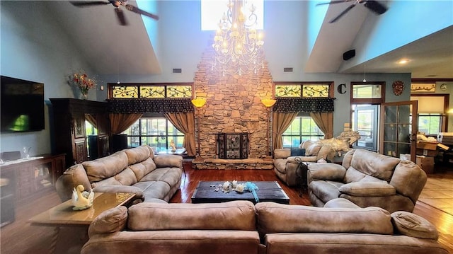 living room with ceiling fan with notable chandelier, a towering ceiling, hardwood / wood-style floors, and a fireplace