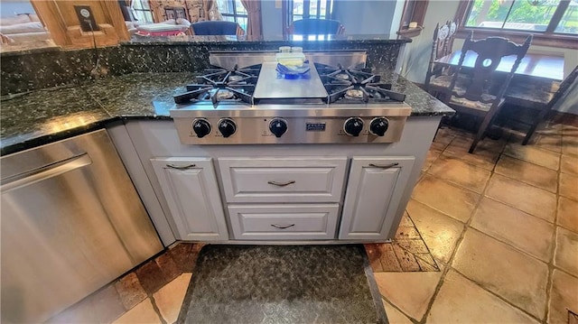 kitchen featuring appliances with stainless steel finishes, white cabinets, light tile floors, and dark stone countertops