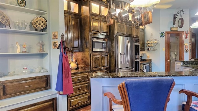 kitchen featuring dark brown cabinetry, appliances with stainless steel finishes, a kitchen breakfast bar, and dark stone counters