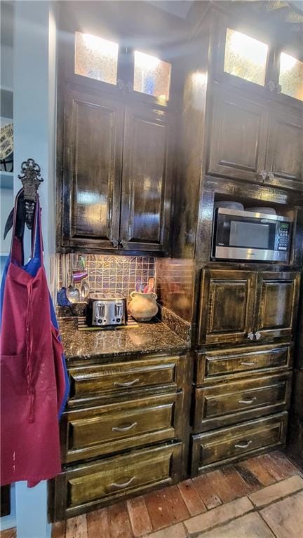 kitchen with backsplash, dark stone counters, and dark brown cabinets