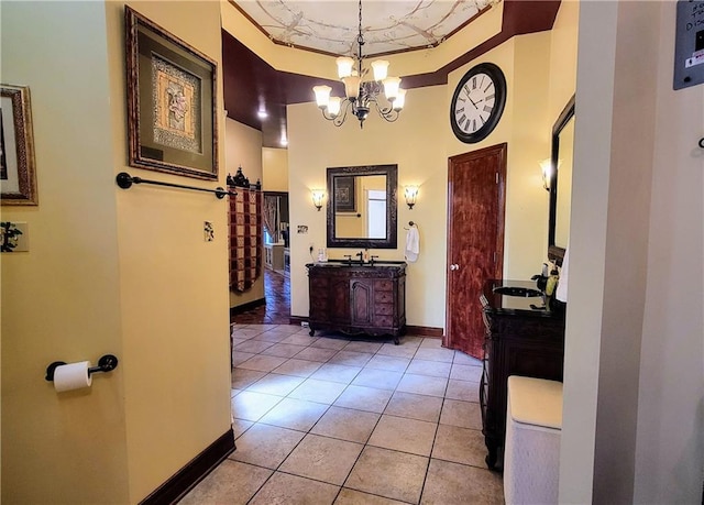 hall with sink, an inviting chandelier, light tile floors, and a raised ceiling