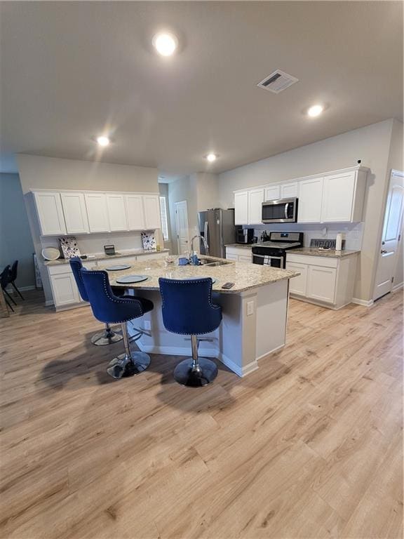 kitchen featuring appliances with stainless steel finishes, a kitchen island with sink, a breakfast bar, and light hardwood / wood-style flooring