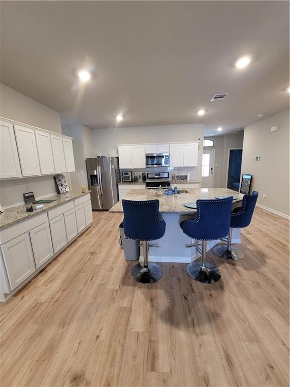 kitchen with light hardwood / wood-style flooring, stainless steel appliances, white cabinetry, and an island with sink