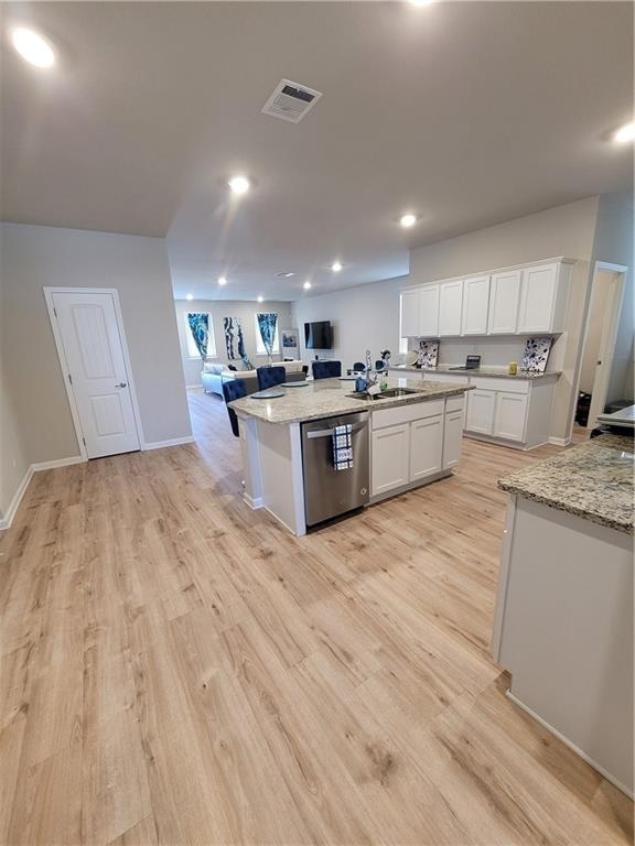 kitchen featuring white cabinets, light wood-type flooring, light stone counters, dishwasher, and an island with sink