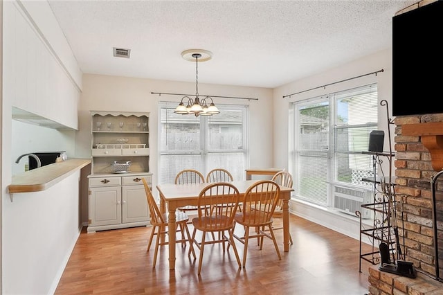 dining room with light hardwood / wood-style floors, a textured ceiling, and a notable chandelier