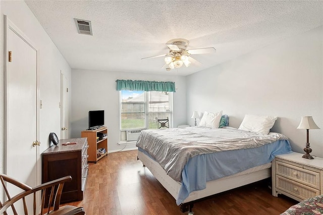 bedroom with a textured ceiling, cooling unit, ceiling fan, and dark wood-type flooring