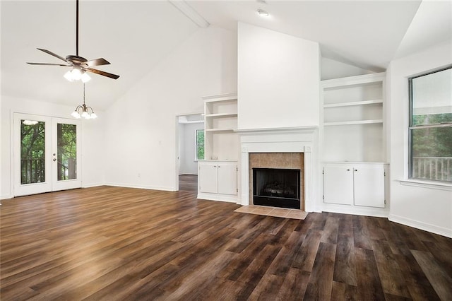 unfurnished living room with french doors, dark hardwood / wood-style flooring, lofted ceiling with beams, a fireplace, and ceiling fan with notable chandelier