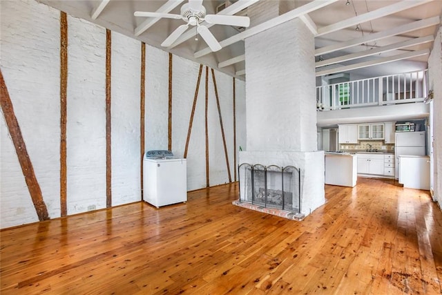 unfurnished living room with ceiling fan, washer / dryer, a large fireplace, a high ceiling, and light wood-type flooring