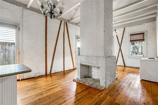 unfurnished living room featuring washer / clothes dryer, an inviting chandelier, beam ceiling, and hardwood / wood-style floors