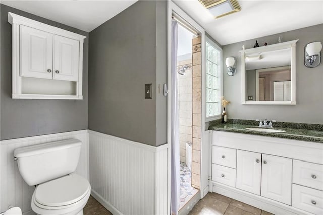 bathroom with a tile shower, vanity, toilet, and tile floors