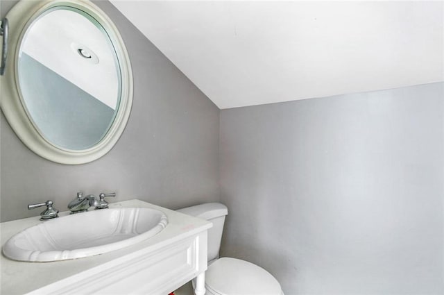 bathroom with toilet, vanity, and lofted ceiling