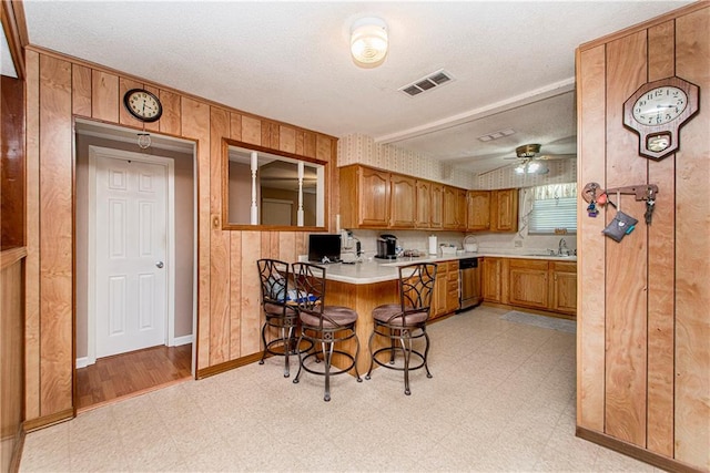 kitchen featuring a breakfast bar area, ceiling fan, dishwasher, wooden walls, and light wood-type flooring