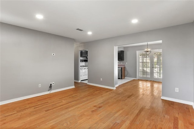 unfurnished living room featuring hardwood / wood-style floors, an inviting chandelier, and french doors