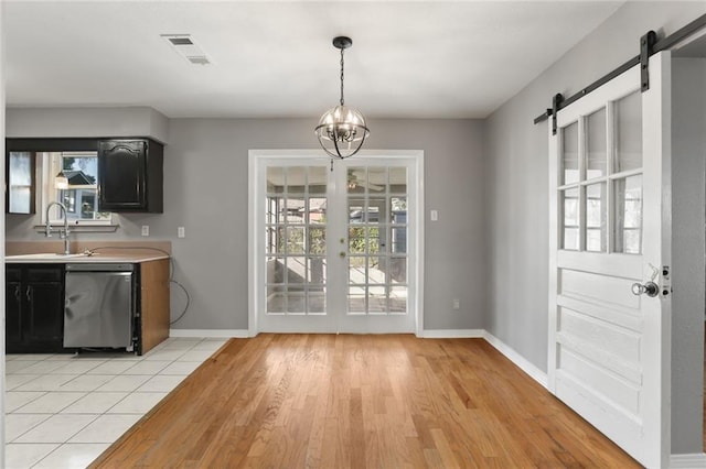 unfurnished dining area with a chandelier, sink, light wood-type flooring, and a barn door