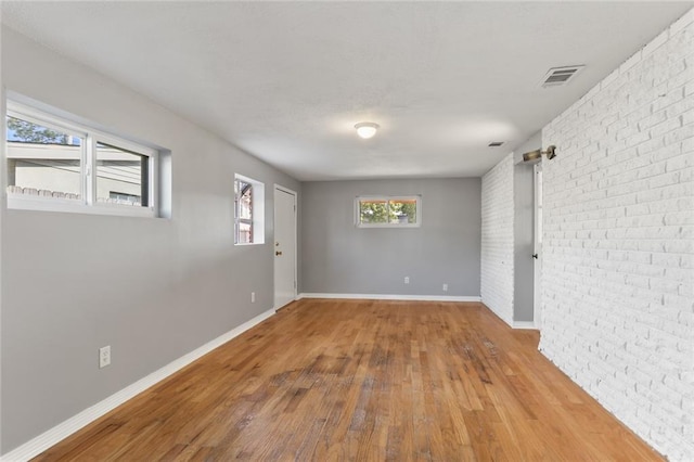 empty room with brick wall and hardwood / wood-style flooring