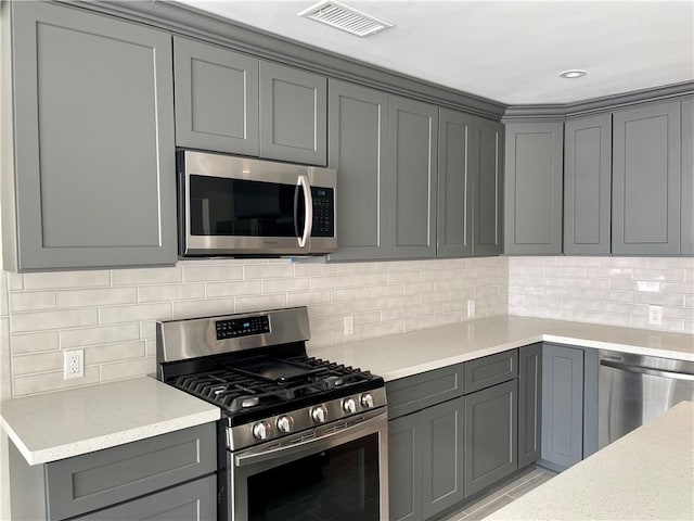 kitchen with light stone counters, backsplash, stainless steel appliances, and gray cabinets