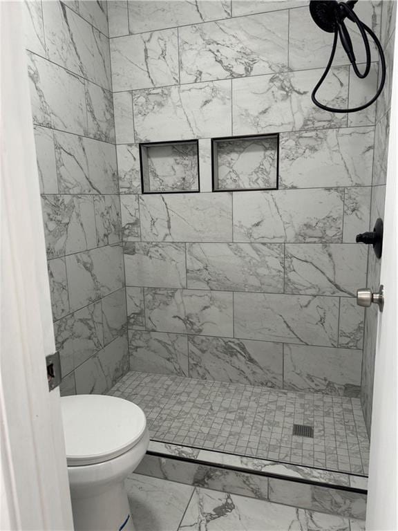 bathroom featuring toilet, tiled shower, and tile flooring