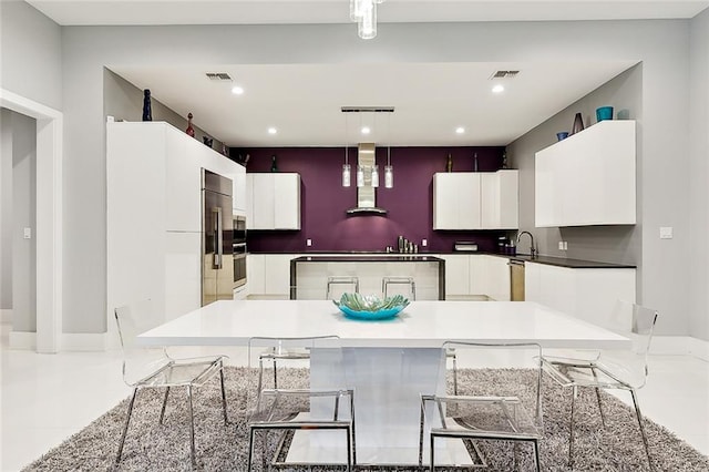 kitchen with wall chimney exhaust hood, a kitchen island, light tile floors, white cabinetry, and stainless steel appliances