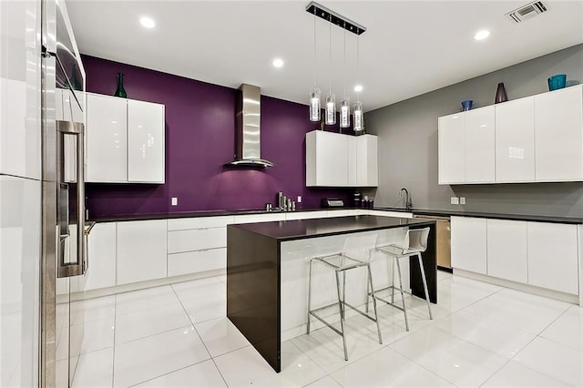 kitchen with hanging light fixtures, light tile flooring, wall chimney exhaust hood, white cabinets, and a center island