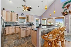 kitchen with high vaulted ceiling, a kitchen bar, ceiling fan, tile flooring, and light brown cabinetry