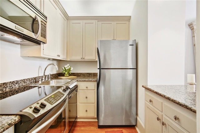 kitchen featuring light hardwood / wood-style flooring, stainless steel appliances, sink, light stone counters, and cream cabinets