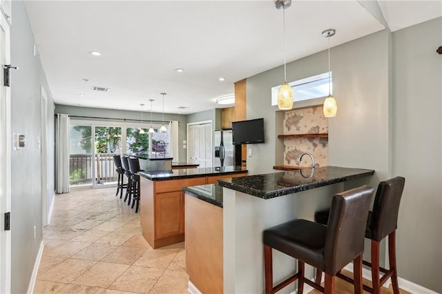 kitchen with a kitchen bar, light tile flooring, decorative light fixtures, stainless steel fridge with ice dispenser, and kitchen peninsula