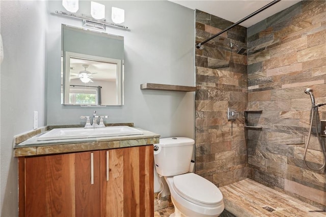 bathroom with tiled shower, toilet, ceiling fan, and vanity